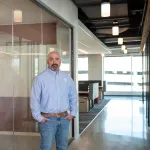 A man in professional wear stands in a hallway.