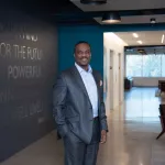 A man in professional wear stands in a hallway.
