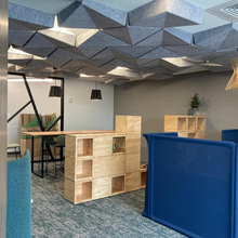 An office setting with geometric ceiling features, a stack of wooden blocks, and a standing desk.