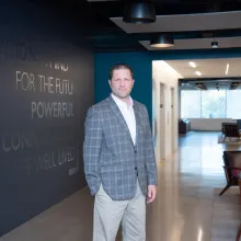 A man in professional wear stands in a hallway.