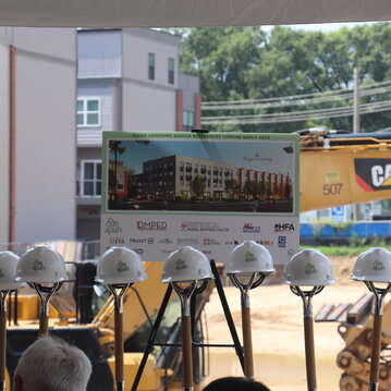 Hard hats sit on top of shovels, signifying the first dig on site. A rendering of the Senior Residences on an easel sits behind the shovels.