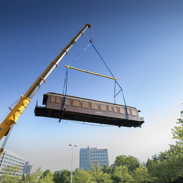A crane lifts a brown railcar high in the air