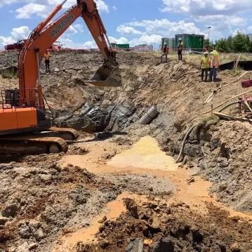 An excavator operates in a construction site, with piles of dirt surrounding it.