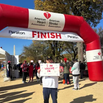 Man holds sign at a fundraising event for heart disease awareness that explains why he's there.