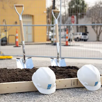 Three hard hats next to a few shovels and a pile of dirt