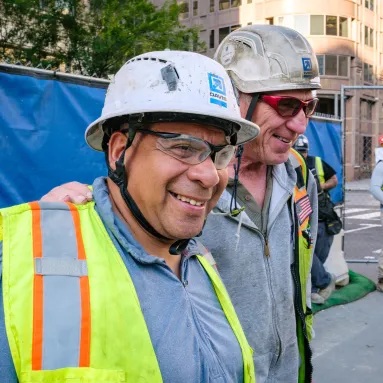 two older men in construction attire smiling to camera