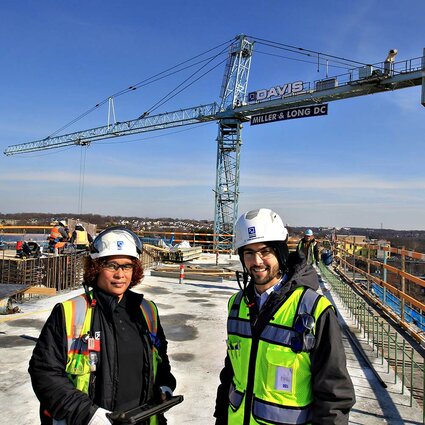 a woman and man wearing hard hats standing in front of a crane
