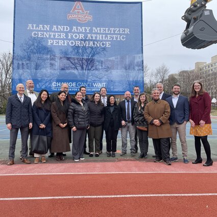 A group of people stand together in front of a sign commemorating the groundbreaking of the Meltzer Center, a new Sports Facility at American University.