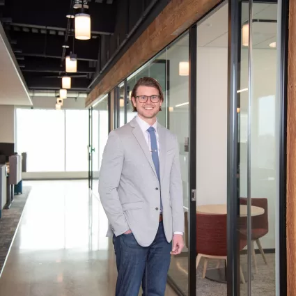 A man in professional wear stands in a hallway.