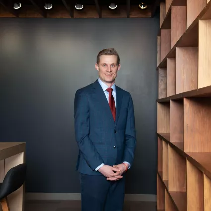 A man in professional wear stands in a hallway.