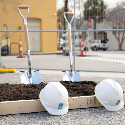 Three hard hats next to a few shovels and a pile of dirt