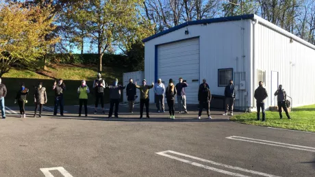 sixteen people lined up in front of white garage