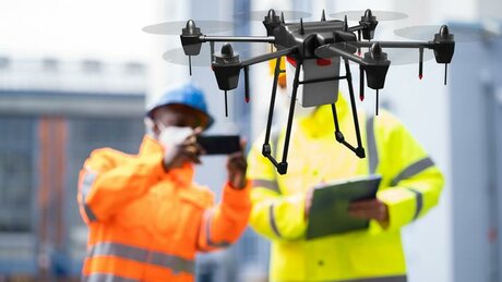 Two construction workers operate a drone