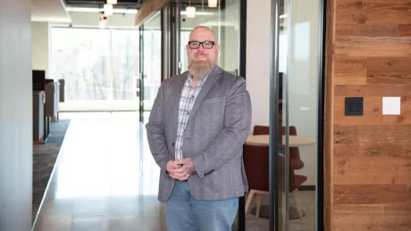 A man in professional wear stands in a hallway.