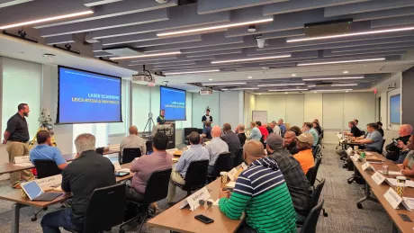 Construction professionals sit at conference room tables listening to a presentation on laser scanning.
