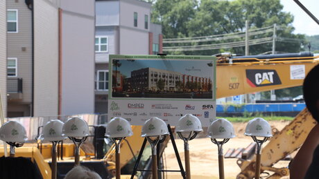 Hard hats sit on top of shovels, signifying the first dig on site. A rendering of the Senior Residences on an easel sits behind the shovels.