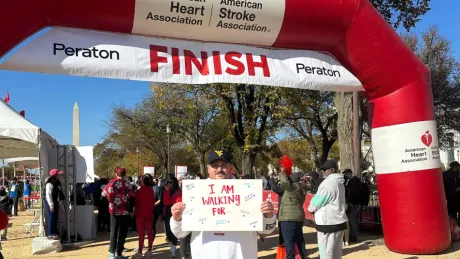 Man holds sign at a fundraising event for heart disease awareness that explains why he's there.