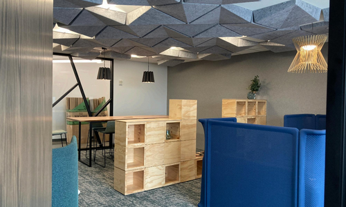 An office setting with geometric ceiling features, a stack of wooden blocks, and a standing desk.