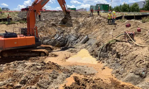 An excavator operates in a construction site, with piles of dirt surrounding it.