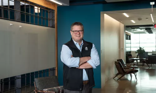 A man in professional wear stands in a hallway.