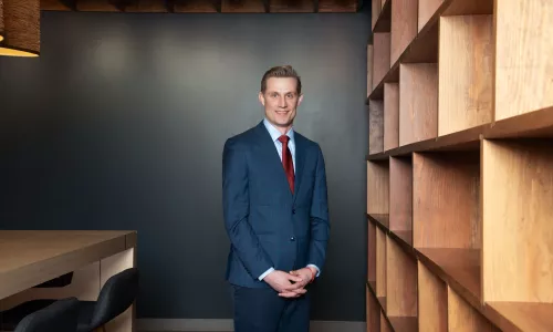 A man in professional wear stands in a hallway.