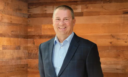 A man in professional wear stands in a hallway.