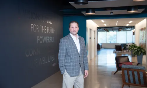 A man in professional wear stands in a hallway.