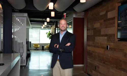 A man in professional wear stands in a hallway.