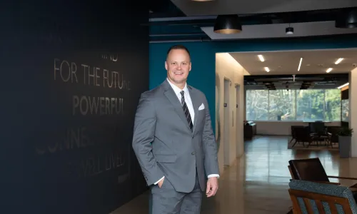 A man in professional wear stands in a hallway.