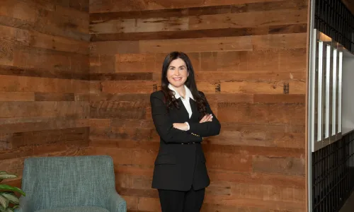 A woman stands in a hallway in professional attire.
