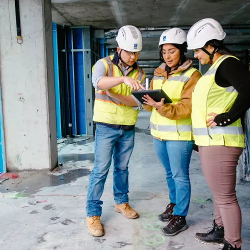 A man and two women on a construction site look at an electronic tablet