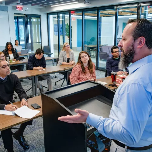 Someone stands at a podium in front of others at their desks.