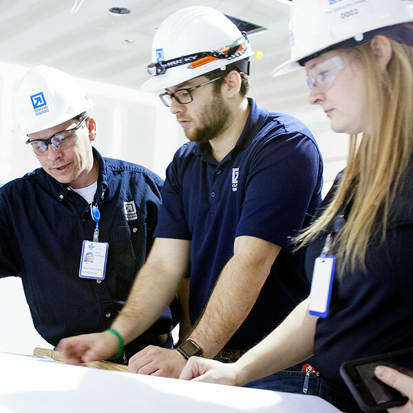 three people wearing hard hats looking at plans