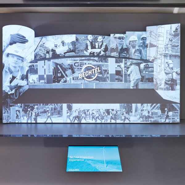 A large screen with a historical photo of the Bechtel corporation, with a smaller screen in front of it