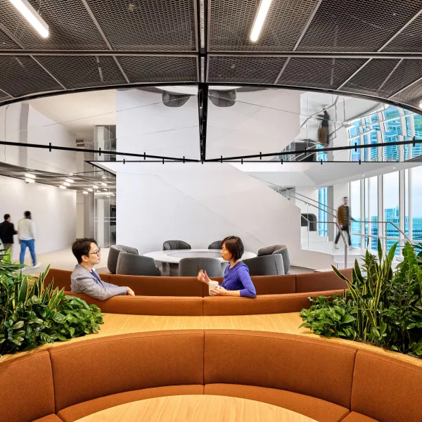 Two office workers sit on a couch and talk to each other.