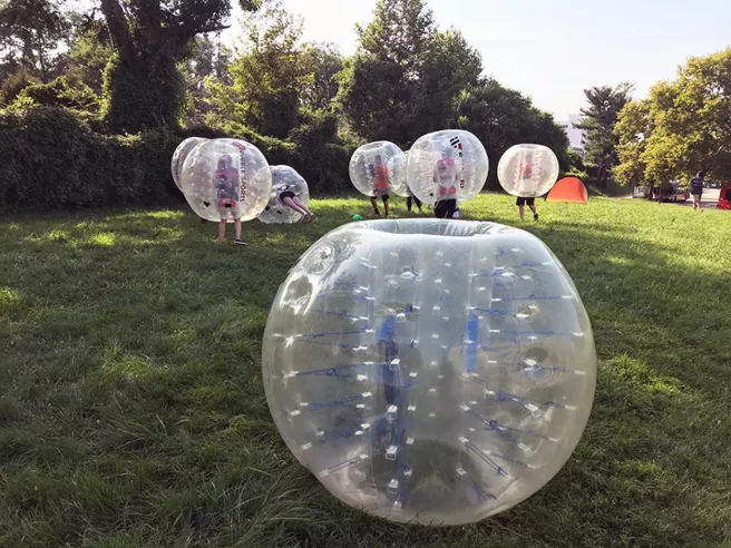 Seven individuals each wearing a plastic bubble playing bubble soccer