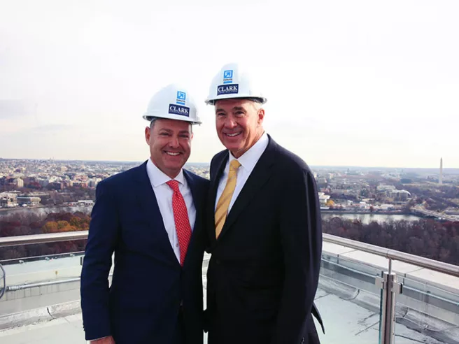 Two men dressed in business suits and hard hats smiling at camera