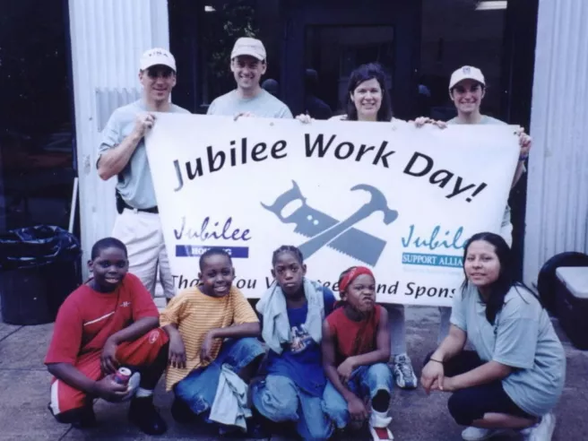4 adults holding banner with 4 children and one adult crouching in front.