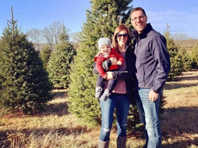 Chad oursler in front of Christmas tree at a tree farm posing with woman and child