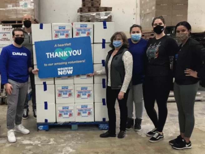 group of people with masks holding a nourish now sign