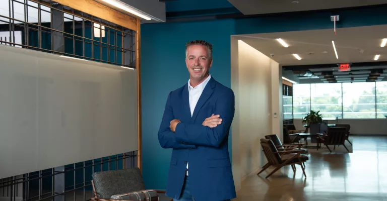 A man in professional wear stands in a hallway.