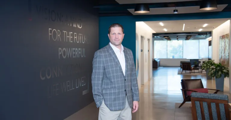 A man in professional wear stands in a hallway.